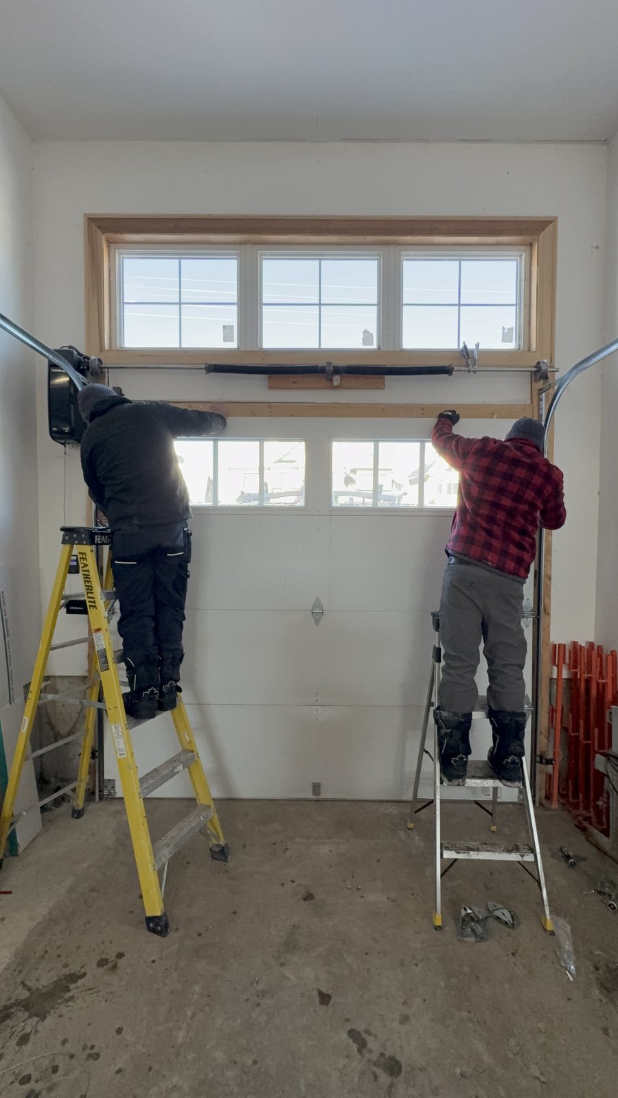 Two Mor Garage Doors technicians on ladders servicing a garage door track and rollers from inside