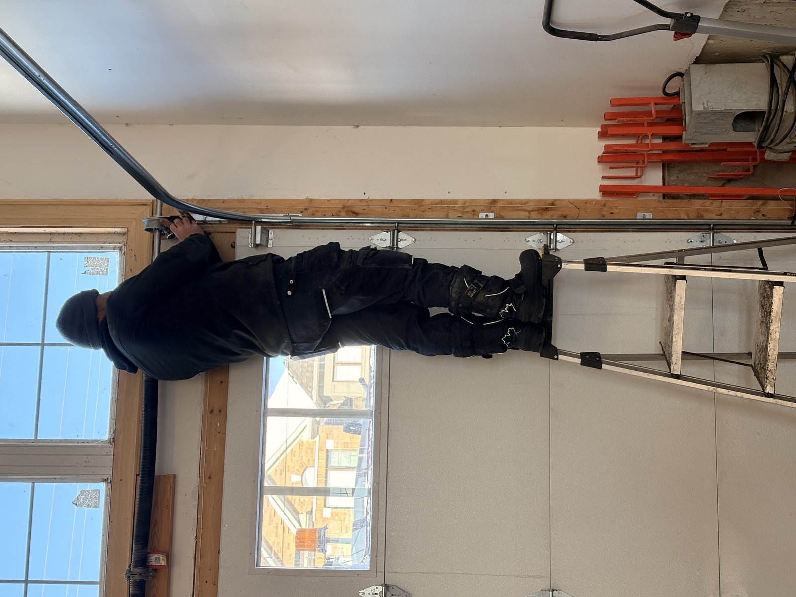A technician on a ladder adjusting the top roller and track of a residential garage door