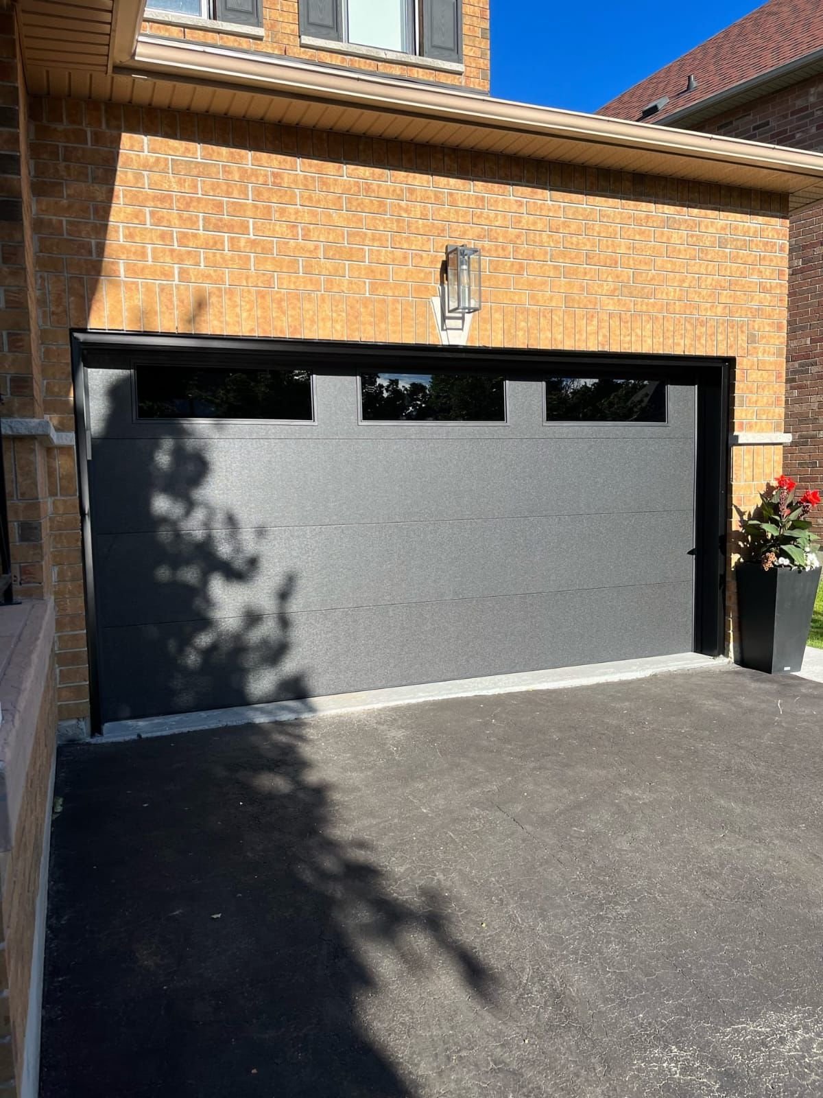Dark sectional garage door with upper windows installed on a brick home