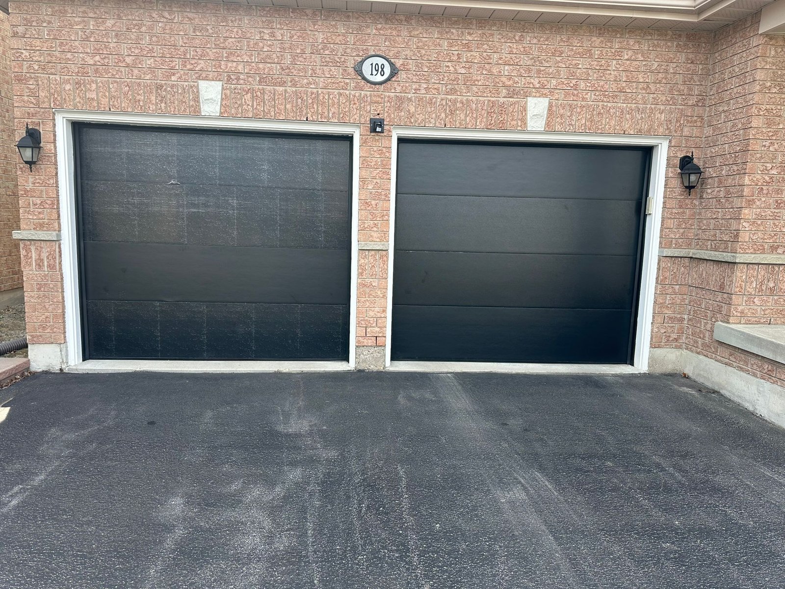 A pair of matching black flush-panel garage doors on a beige brick home