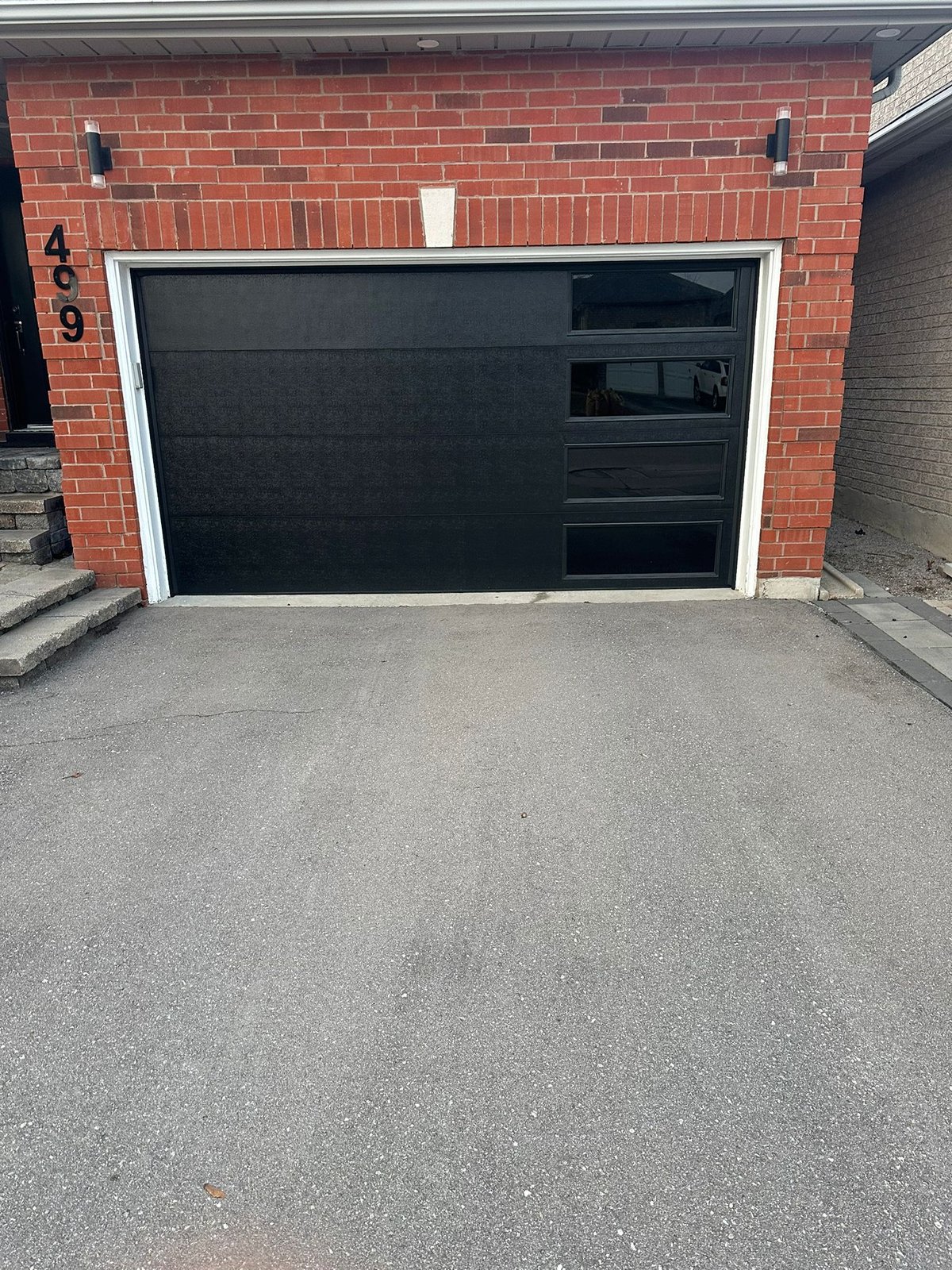 Black garage door with windows along one side on a red-brick home