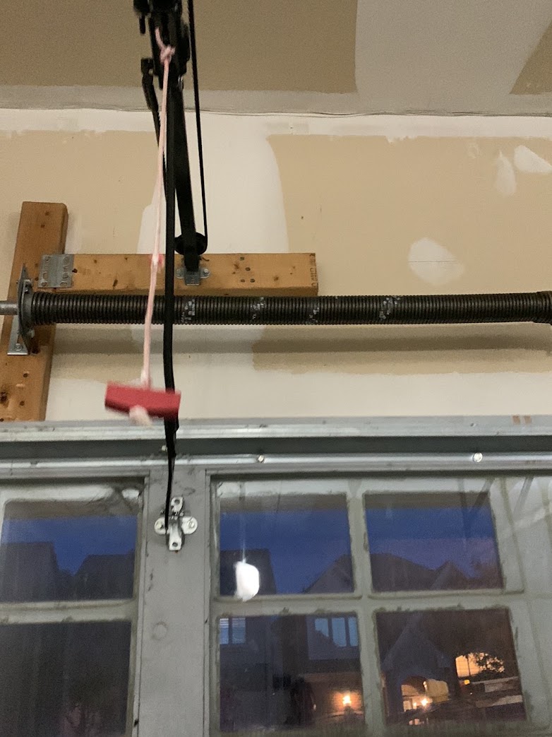 A close-up of a garage door torsion spring and winding shaft on the header during a repair